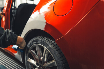 Part of a red car covered with automotive filler. Professional mechanic at work. Repairing and...