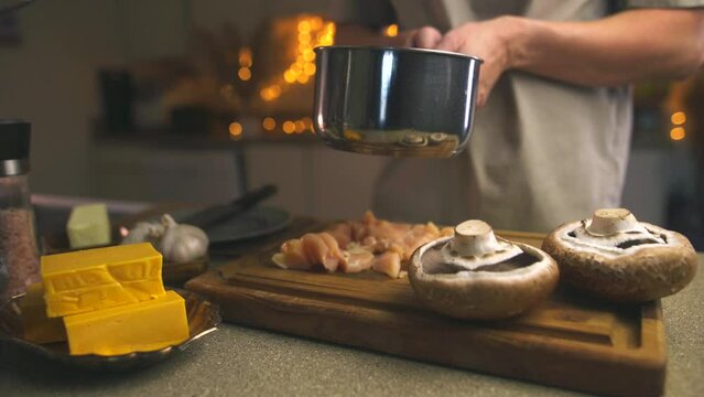 Video. A man prepares an appetizing dish in the kitchen. Place the cut pieces of meat into the pan. Mushrooms, cheese, butter, spices, garlic are on the kitchen table. Simple and delicious recipes.
