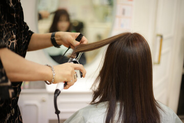 女性の髪にヘアアイロンをかける男性美容師