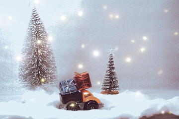 Christmas concept, small toy truck in retro style with New Year's gifts in the back of a truck with sparkling lights on a blurred background. Delivery.