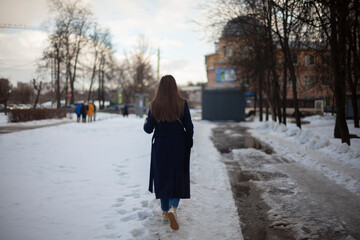 Girl walks down street in winter. Woman in winter in city. Bad road in yard in Russia.