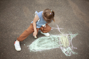 Child draws on asphalt with chalk. Child plays outside. Creative abilities of baby.