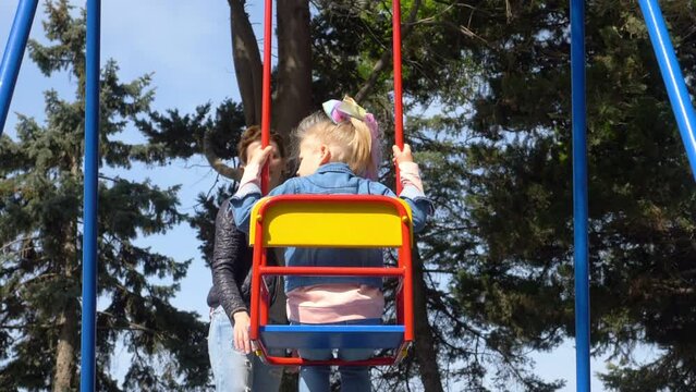 childhood, fun - young mom pushes her little gitl on the swing at park