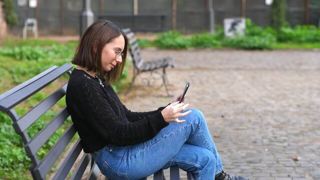 technology, device - young woman on park bench smiles looking at photos on ipad