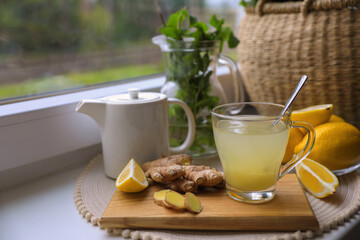 Glass of aromatic ginger tea and ingredients near window, space for text