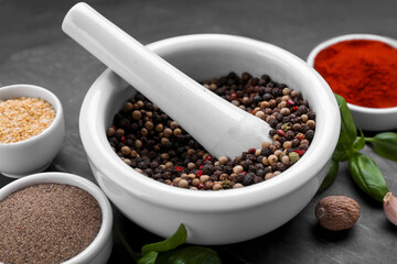 Mortar with pestle and different spices on black table, closeup