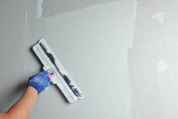 Professional worker plastering wall with putty knife, closeup