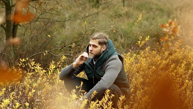 Man sitting in a field with yellow flowers while smoking tabacco.