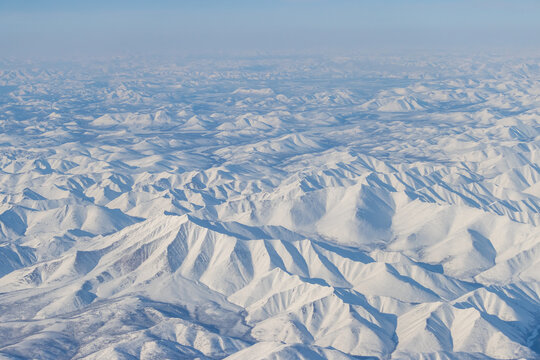 Aerial view of snow-capped mountains and river. Winter snowy mountain landscape. Air travel to the far North of Russia. Mount Nuh, Kolyma Mountains, Magadan Region, Siberia, Russian Far East.