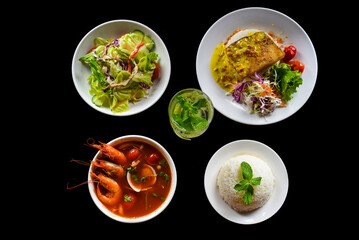 Lunch set made of tom yum soup, salad, grilled basa fish, rice, lemonade on black background