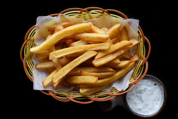 French fries in a basket with creamy garlic sauce on black background top view
