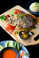 Red perch grilled in batter with vegetables and greens on wooden chop board isolated on black...