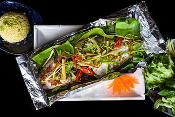 Parrot fish grilled in Vietnamese style with vegetables and rice isolated on black background top...