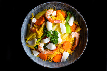 Seafood with noodles in a bowl isolated on black background top view