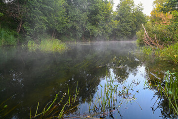 The river is covered with morning fog at sunrise, surrounded by a dense green forest. Wild nature. Active weekend vacations wild nature outdoor.