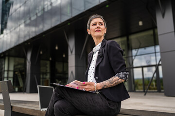 One woman mature senior sit in front of modern business building wait