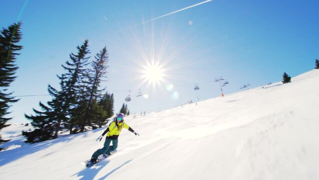 girl snowboarding on slopes and falling. female snowboarder in european ski center. front view. clear blue sky.