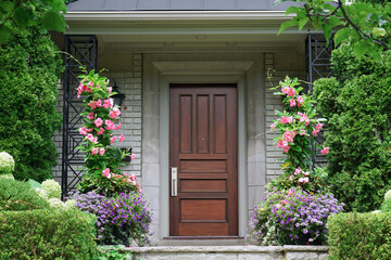 Modern style wood grain front door of house, surrounded by bushes and flowers