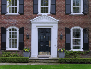 Front door of traditional two story brick house with black shutters beside the windows