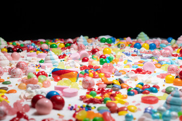 Fototapeta na wymiar Multi-colored candy balls on icing sugar table. Candy sweets background made of assorted chocolate coated and jelly beans. Various shaped delicious sugary treats. Holiday festive background.