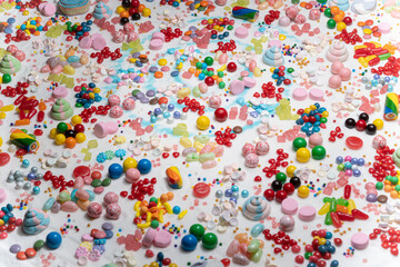 Fototapeta na wymiar Multi-colored candy balls on icing sugar table. Candy sweets background made of assorted chocolate coated and jelly beans. Various shaped delicious sugary treats. Holiday festive background.