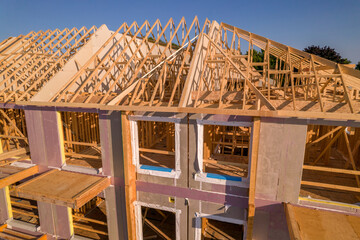 Housing gables roof on wood sticks. Wooden city home under construction at golden hour. New...