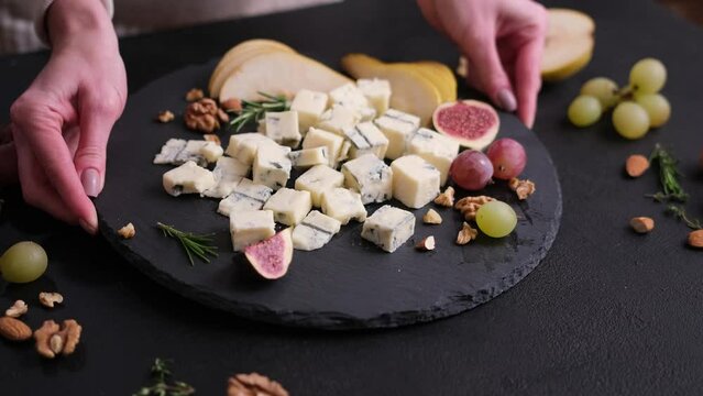 Woman puts stone serving board with Sliced Traditional Italian Gorgonzola cheese on a table