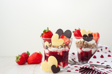 Two glasses with a sweet breakfast of cream cheese and pureed berries on a white wooden table. Side view. Strawberry valentine's day dessert decorated with heart-shaped chocolate and ripe berries