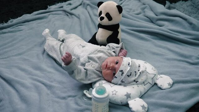Cute newborn girl lying on gray blanket with toy and bottle of milk