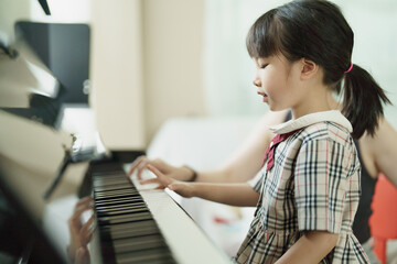 Asian girl kid learning or practicing piano at school.