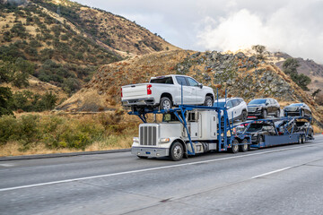 Classic powerful big rig car hauler semi truck transporting crossovers on the modular semi trailer climbing uphill on the multiline mountain highway road