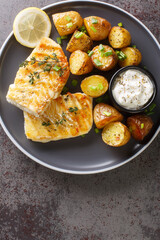 Healthy dinner of grilled white fish with baked potatoes close-up in a plate on the table. Vertical top view from above