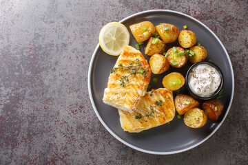 Grilled fish cod fillet with thyme served with baked potatoes, cream sauce and lemon on the table....