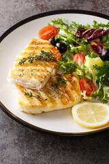 Grilled cod fillet served with fresh vegetable salad close-up in a plate on the table. Vertical