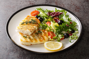 Spicy grilled cod fish fillet with fresh vegetable salad and leaf lettuce mix and lemon close-up in a plate on the table. Horizontal