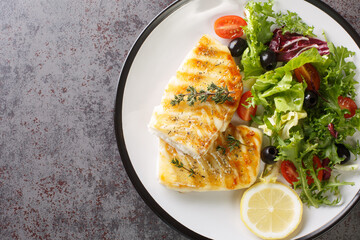 Delicious healthy grilled cod fish with fresh salad of tomatoes, olives, lettuce mix and lemon...