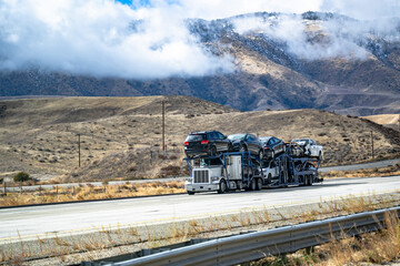 Industrial classic big rig white car hauler semi truck transporting heavy cars on the modular semi...