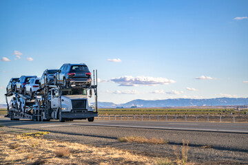 Industrial grade low cab big rig semi truck transporting cars on the hydraulic semi trailer driving...