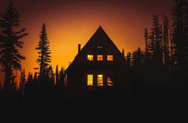 View of cabin in the woods with lit windows at sunset