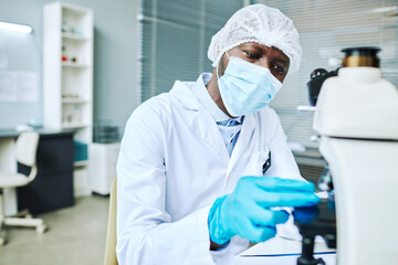 Portrait of focused black man wearing face mask while doing research in medical laboratory