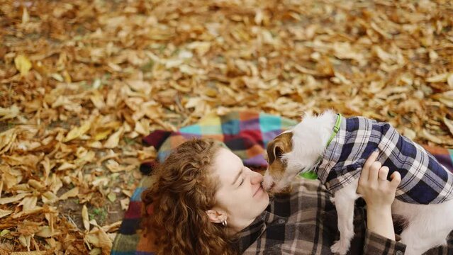 Woman laying on a plaid with her jack russell terrier puppy in autumn park and having fun