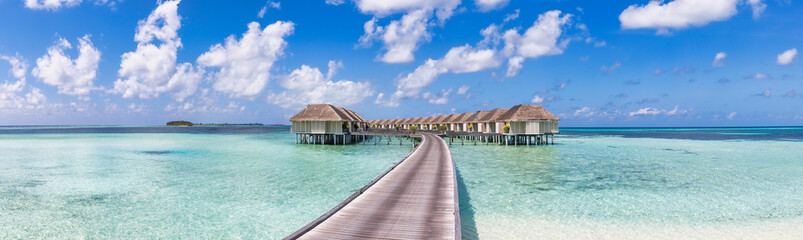 Obraz premium Amazing Maldives, travel panorama. Luxury resort villas seascape with sunny blue sky, tranquil ocean lagoon. Wooden walkway. Tropical paradise inspiration. Wallpaper banner exotic vacation destination
