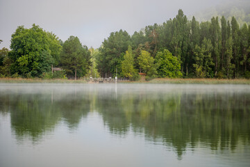 Fototapeta na wymiar Idyllic landscape about a lake with some fog and surrounded by green trees