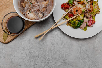 Shrimp udon soup and seafood salad on a gray background. View from above.

