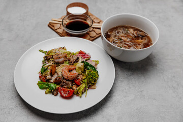 Shrimp udon soup and seafood salad on a gray background. Side view.