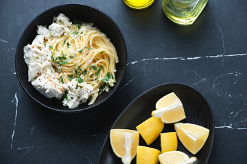 Bowl with lemon and ricotta spaghetti on a black marble background, horizontal shot with space, view from above
