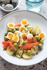 Closeup of salad with baby potato, red fish fillet, quail eggs and green olives, vertical shot, selective focus