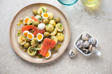 Plate with baby potato, smoked trout and quail eggs salad, above view on a beige stone background, horizontal shot
