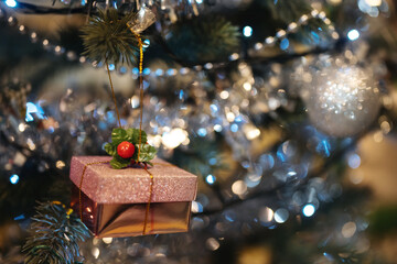 A box with a gift hangs on a Christmas tree decorated for the New Year and Christmas in the evening with a garland.