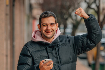 young man on the street with mobile phone excited celebrating success in warm clothes